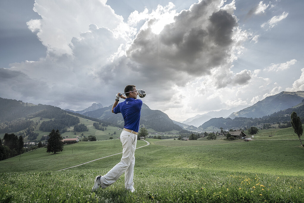 <p>Ein Golfspieler in weissen Hosen und blauem Hemd, spielt Golf vor Bergpanorama.</p>