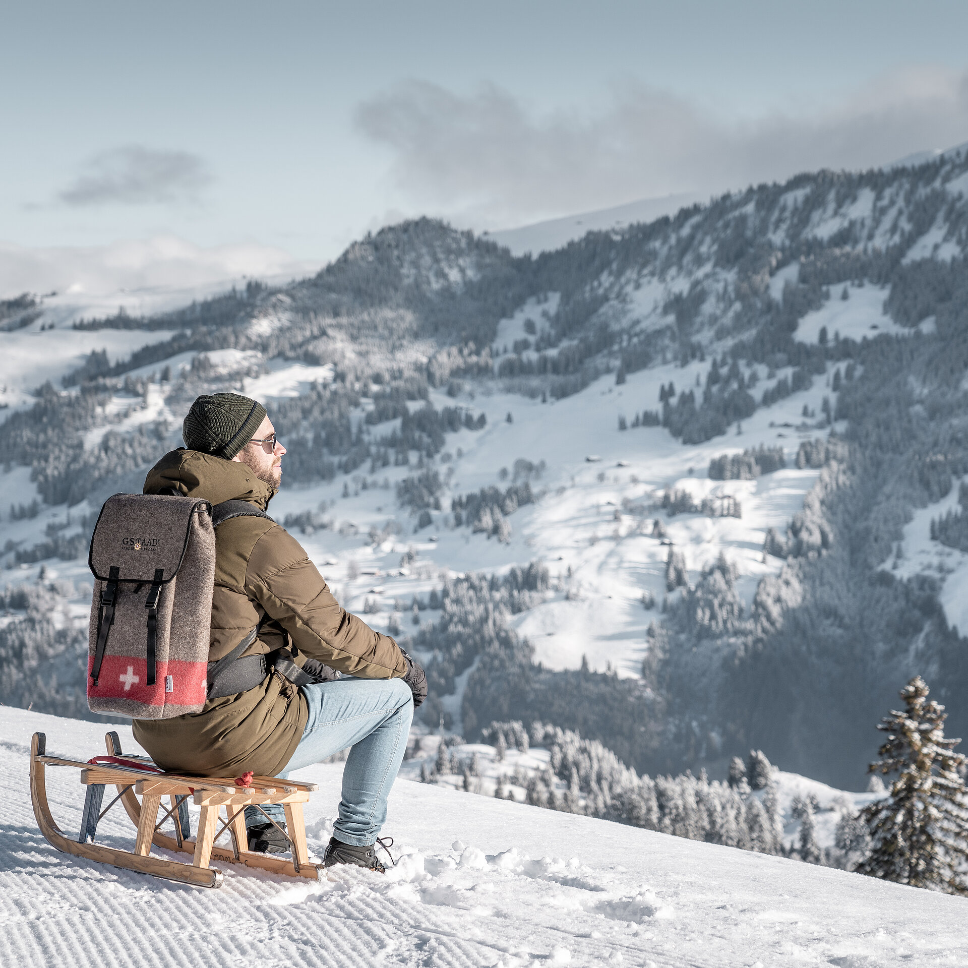 <p>Person sitzend auf einem Holzschlitten vor verschneiter Bergkulisse.</p>