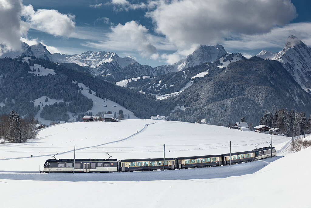 <p>Der Belle Epoque Zug, welcher vor einer verschneiten Berglandschaft vorbeifährt.</p>