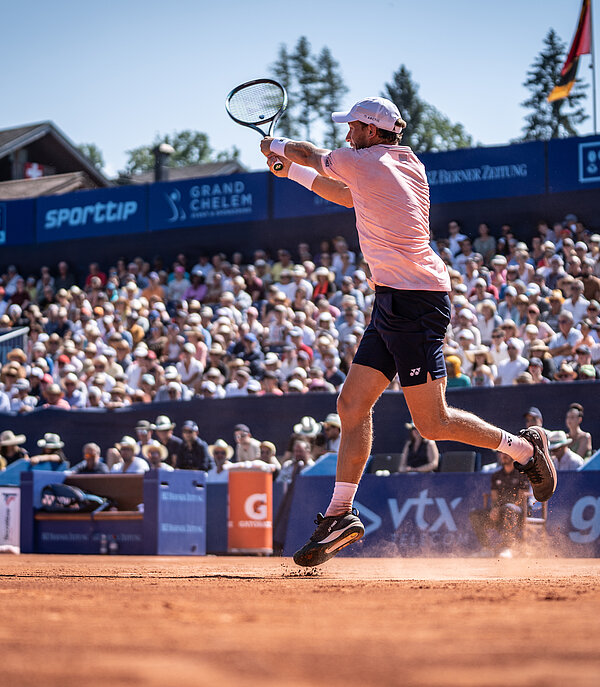 Tennisspieler Casper Ruud schlägt Ball zurück auf dem Tennisfeld in Gstaad, Publikum im Hintergrund schaut gespannt zu.
