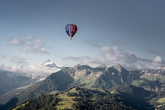 Un ballon coloré flotte au-dessus du paysage montagneux verdoyant du Saanenland.
