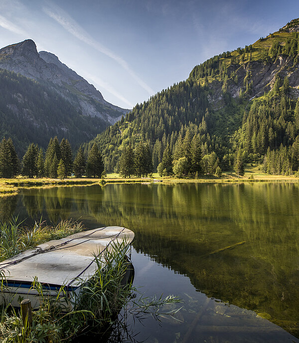 Lake Lauenen in autumn with mountains in the background. A rowing boat can still be seen in the foreground.