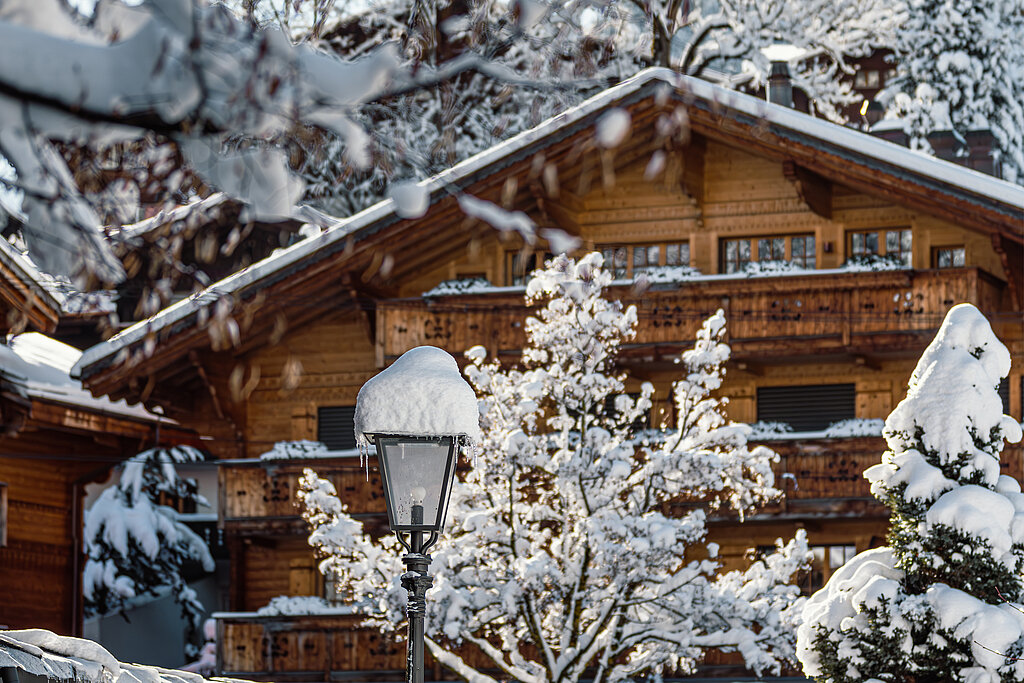 <p>Ein typisches vierstöckiges Holzchalet mit Balkonen zwischen schneebedeckten Bäumen.</p>