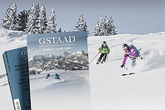 Zwei Skifahrer auf der Abfahrt durch Pulverschnee. Im Hintergrund verschneite Tannen. Im Vordergrund zwei Keycards Skidatenträger mit dem Gstaad Logo und einem Bild einer Skipiste mit Bergpanorama und zwei Skifahrern.