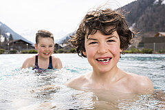 Deux enfants dans l’eau d’une piscine extérieure, avec paysage de montagne en arrière-plan.