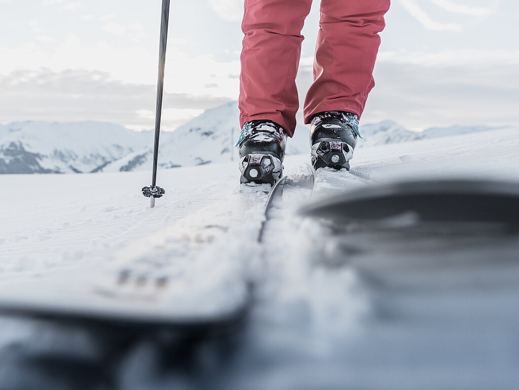 <p>Nahaufnahme von Ski, im Hintergrund die Skipiste und verschneite Bergen.</p>