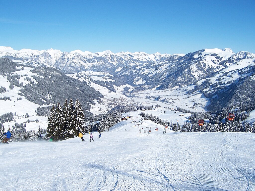 <p>Skipiste von oben Richtung Tal fotografiert, im Hintergrund liegt Zweisimmen umgeben von verschneiten Bergen.</p>