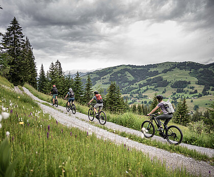 Eine Familie ist oberhalb Saanenmöser auf einer Naturstrasse auf einer Biketour. Auf der anderen Talseite sieht man das Rellerli.
