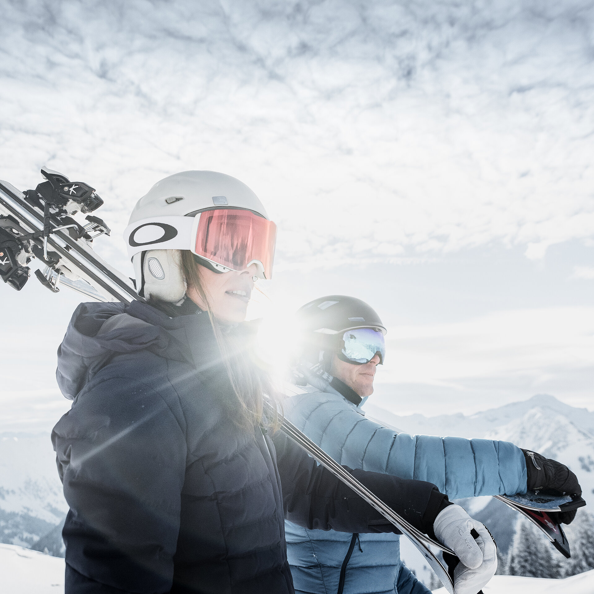 Zwei Skifahrer tragen die Skis bei Sonnenschein vor einer wunderschönen Landschaft.