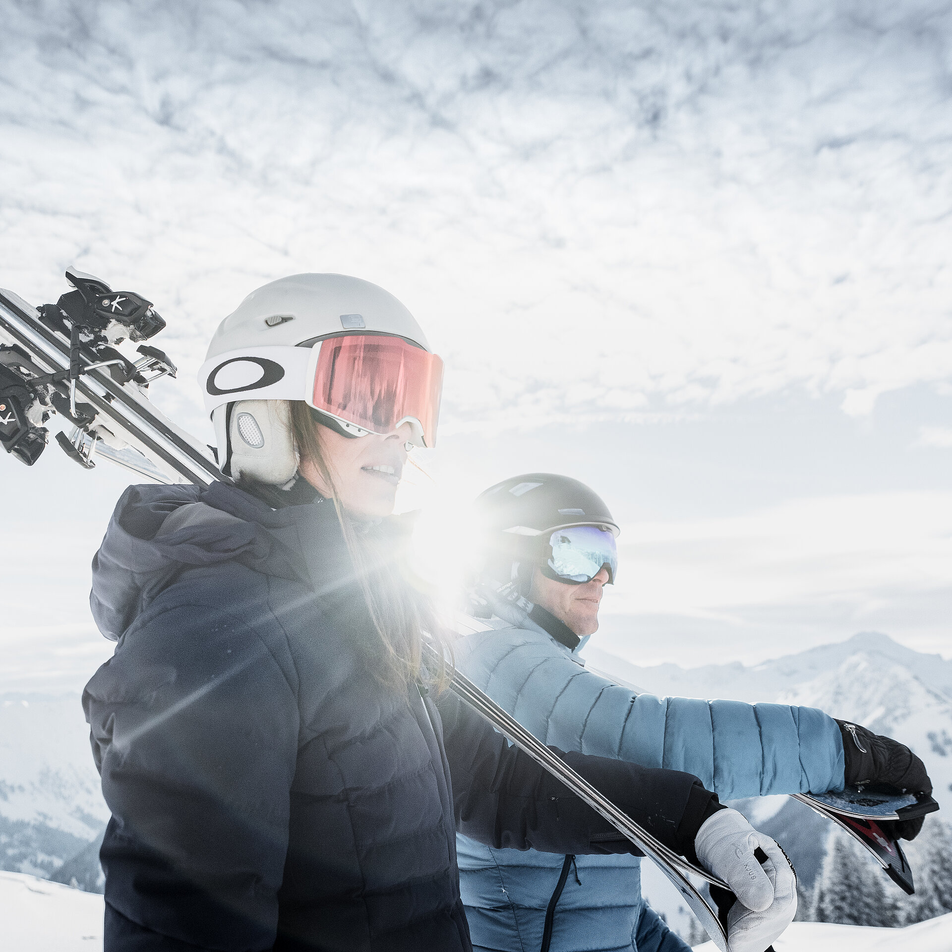 <p>Zwei Skifahrer tragen die Skis bei Sonnenschein vor einer wunderschönen Landschaft.</p>