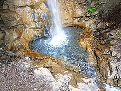 Ein Wasserfall mit einem kleinen herzförmigen Wasserbecken in felsiger Umgebung.