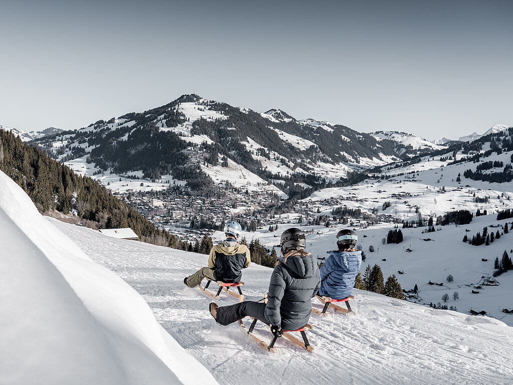 <p>Drei Personen die den Schlittelweg nach Gstaad runter fahren mit schönem Panorama Blick auf die Ferienregion Gstaad.</p>