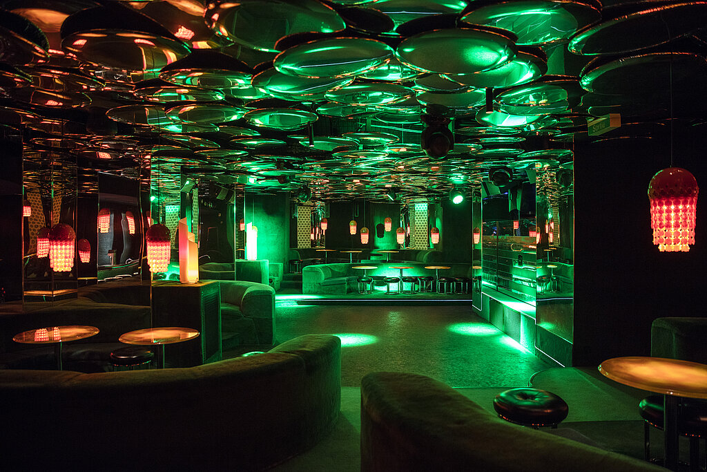<p>Nachtclub mit Lounges, orangenen Lampen und grünem Licht über der Tanzfläche.</p>