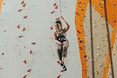 Eine Kletterin hängt an einem Seil vor einer Kletterwand.