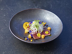 Tiefer schwarzer Teller mit einem Fischgericht und Verzierung.&nbsp;