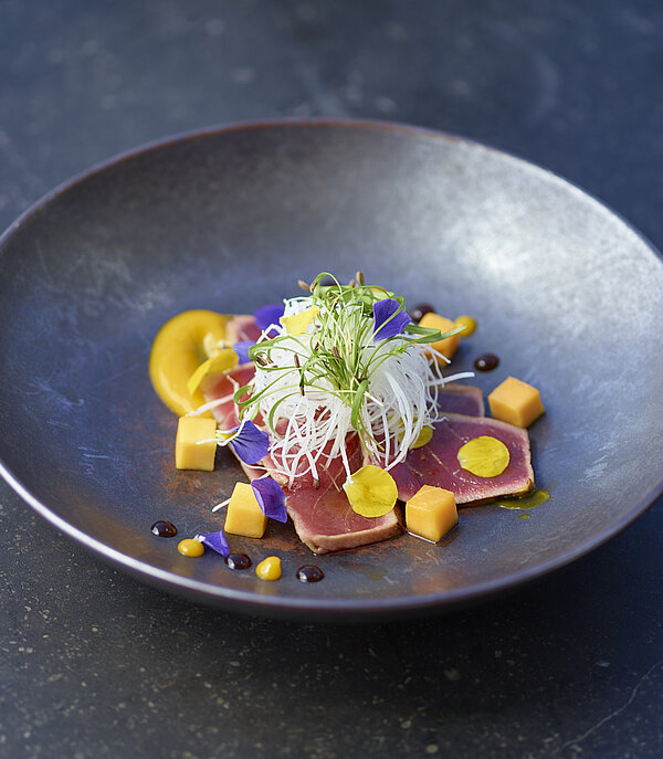  Deep-rimmed black plate with a fish dish and garnishings.&nbsp;