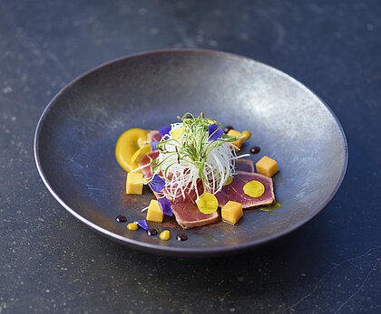 Tiefer schwarzer Teller mit einem Fischgericht und Verzierung.&nbsp;