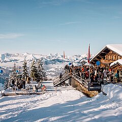 A group of people on a snowy terrace next to a mountain restaurant.