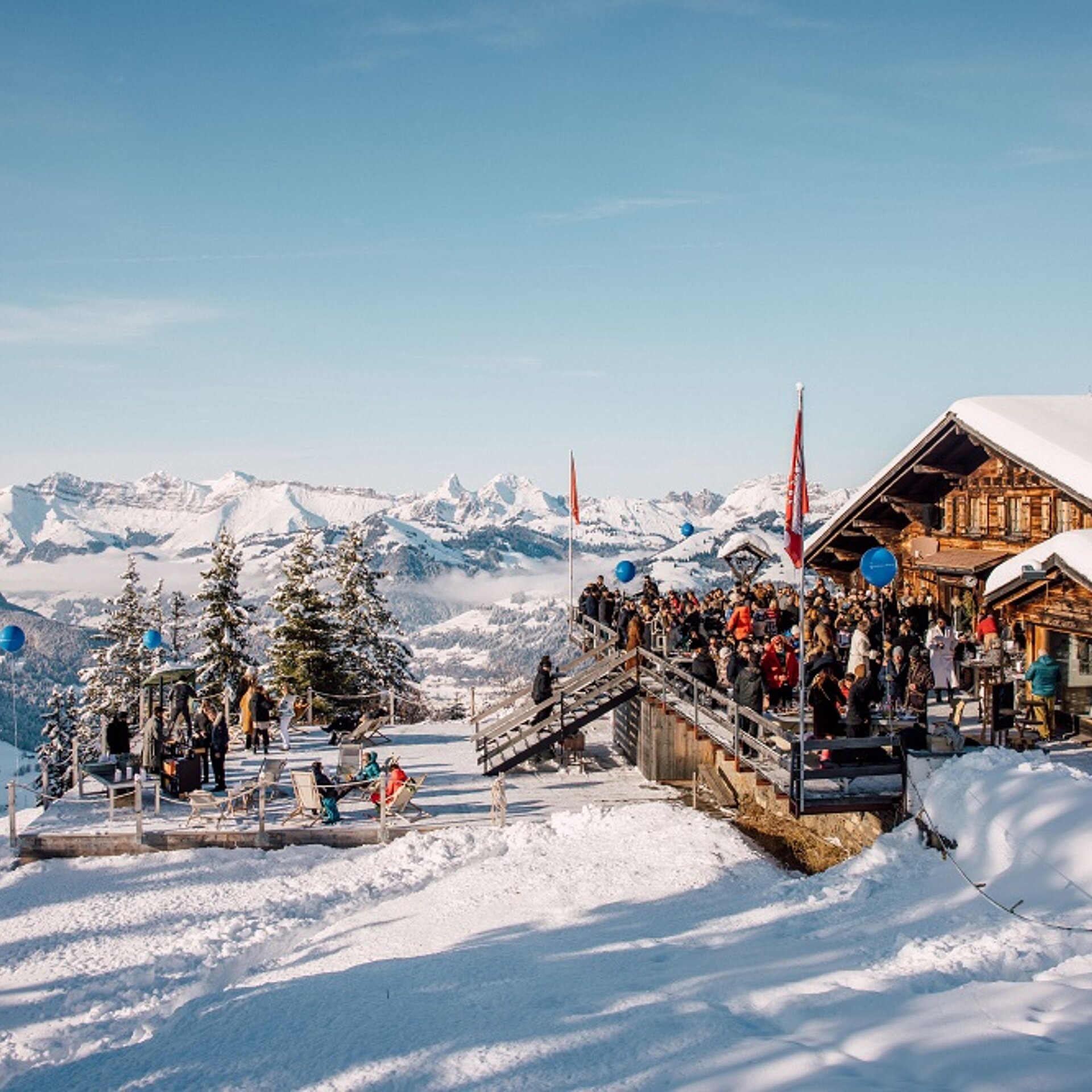 <p>Eine Gruppe von Menschen auf einer Terrasse im Schnee neben einem Bergrestaurant.</p>