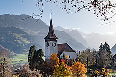 Ein Dorf mit einer grossen Kirche und von farbigen Bäumen umgeben.