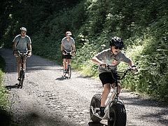 Eine Familie hat sichtlich Spass mit der Trottinettabfahrt durch den Wald
