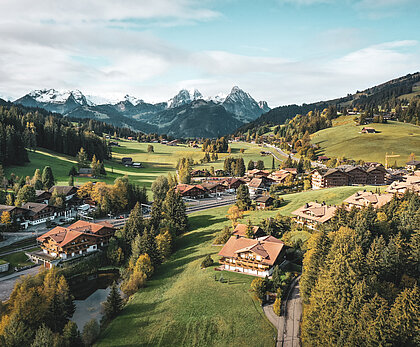 Aus der Vogelperspektive sieht man das Dorf Saanenmöser im Sommer. Die Flächen rund ums Dorf sind grün und im Hintergrund sieht man höhere Berge.