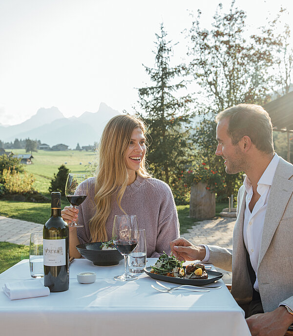 Un couple est assis à une table dressée en plein air devant un chalet au cœur des montagnes.