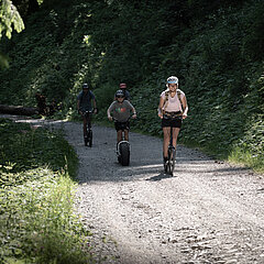 People ride down the mountain on a scooter in a summery atmosphere.