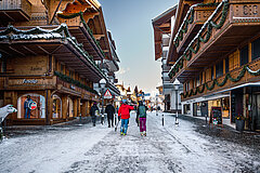Zwei Personen in Skiausrüstung laufen durch die verschneite Promenade in Gstaad.