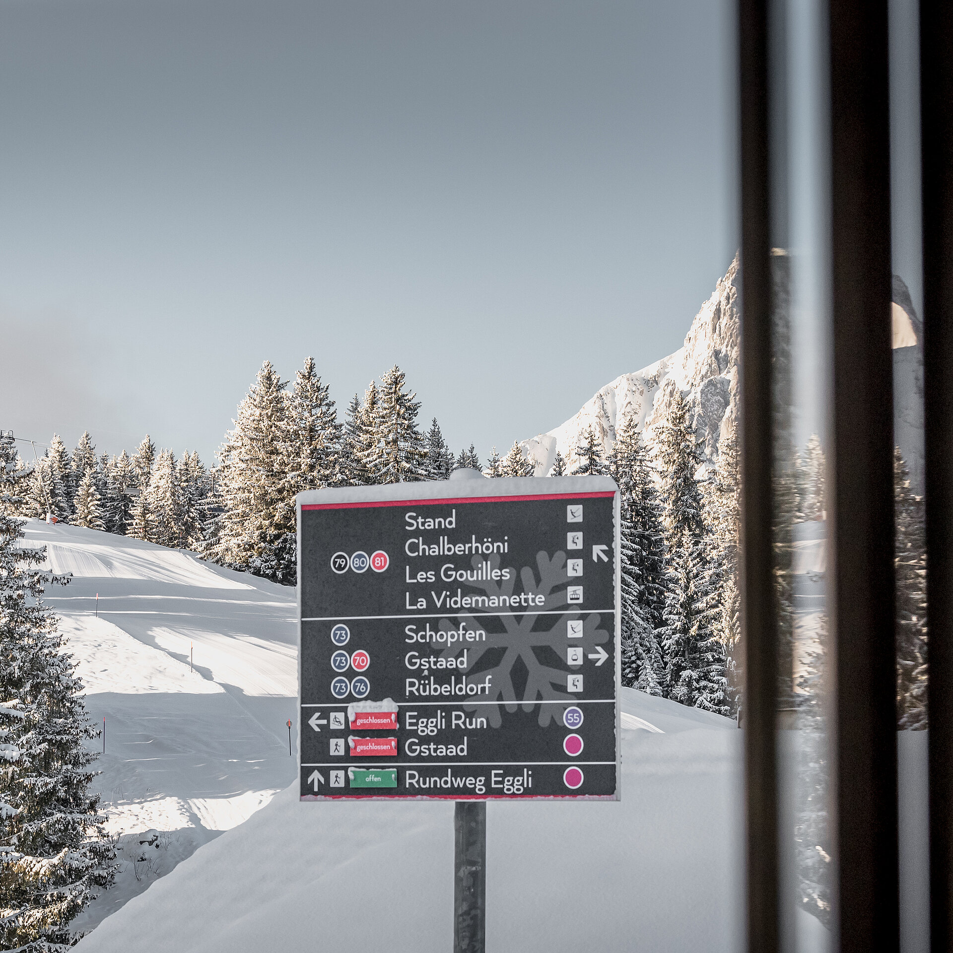 Weisse Bergkulisse mit einem Wegweiser Schild in gross und schwarz und diversen Posten vor der Kulisse.&nbsp;