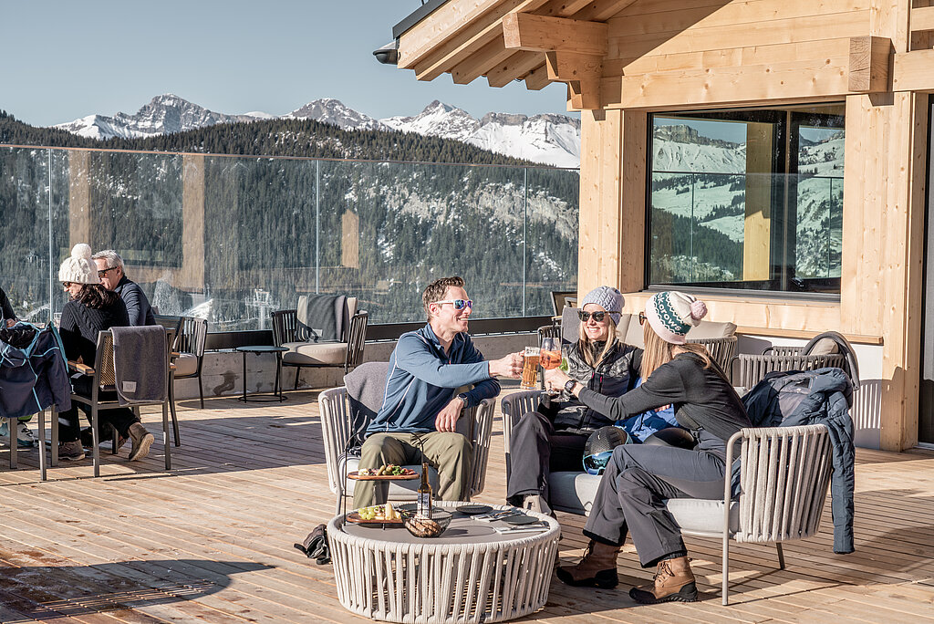 <p>Drei Personen sitzen auf der Terrasse eines Bergrestaurants und trinken etwas.</p>