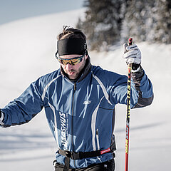  Un skieur de fond vêtu de bleu fixe le sol dans un paysage enneigé.