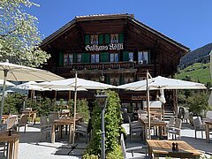 Altes braunes Chalethaus mit weissen Sonnenschirmen im Garten.