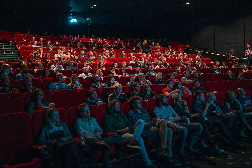 <p>Kinosaal mit roten Sesseln und vielen Menschen die auf die Leinwand schauen.</p>