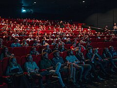 Salle de cinéma avec des fauteuils rouges et beaucoup de gens qui regardent l'écran.