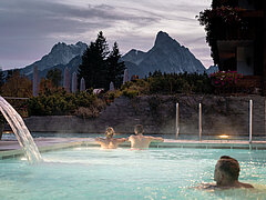 Trois personnes se baignent dans un jacuzzi en plein air, avec les montagnes en arrière-plan.