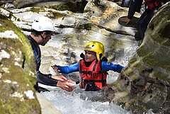 Un enfant et un homme dans une eau de montagne avec néoprène et équipement de canyoning.