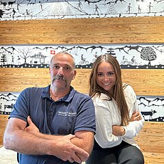 Walter Reichenbach und Selina Riegert (Mitarbeiterin GST) strahlen in die Kamera&nbsp;vor einer Scherenschnitt Wand.