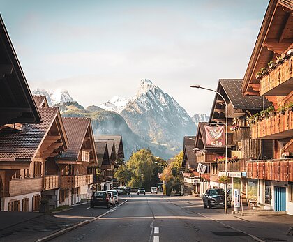 Eine malerische Dorfstraße mit traditionellen Chalets und Blick auf majestätische Berge im Hintergrund. Die Umgebung ist ruhig und idyllisch, ideal für einen entspannenden Aufenthalt.