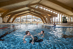 Ein Paar schwimmt in einem Hallenbad, draussen ist es Winter.