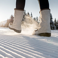Detailansicht von Winterstiefeln auf frisch präpariertem Winterwanderweg.