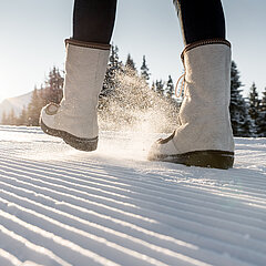 Detailansicht von Winterstiefeln auf frisch präpariertem Winterwanderweg.