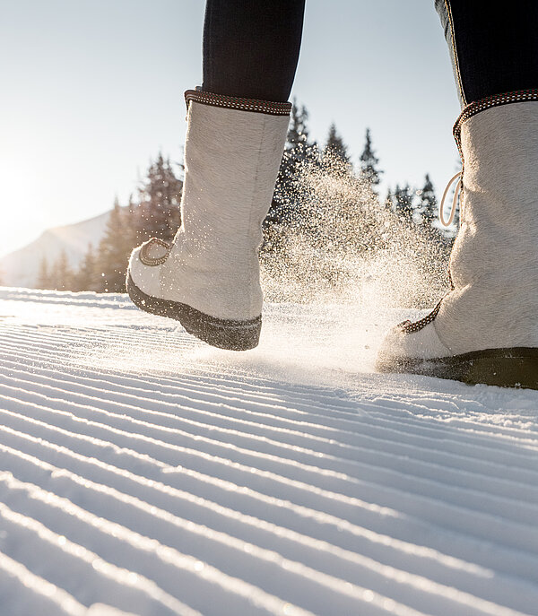Detailansicht von Winterstiefeln auf frisch präpariertem Winterwanderweg.