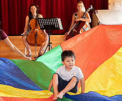 La photo montre plusieurs enfants participant à un concert avec des musiciens en arrière-plan.