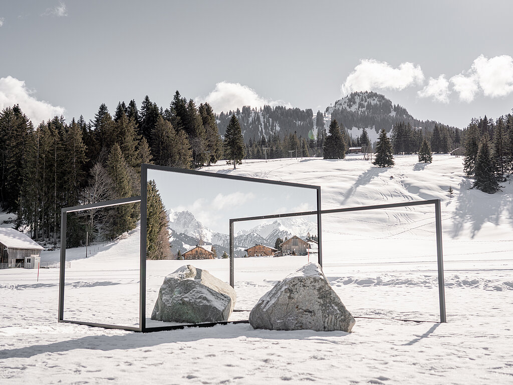 <p>Kunstausstellung auf einer verschneiten Wiese mit Spiegeln und Steinen</p>