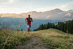 Un homme en tenue de sport rouge et bleue fait son jogging sur un sentier de randonnée dans l'ambiance matinale.