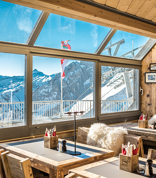 Table and chairs in the La Videmanette mountain restaurant with a view of a snowy mountain landscape.