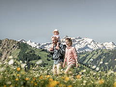 Familie mit einem kleinen Kind wandert durch die Blumenwiesen bei sommerlichem Wetter. 