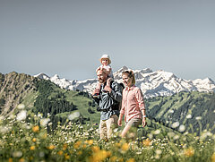 Familie mit einem kleinen Kind wandert durch die Blumenwiesen bei sommerlichem Wetter.&nbsp;
