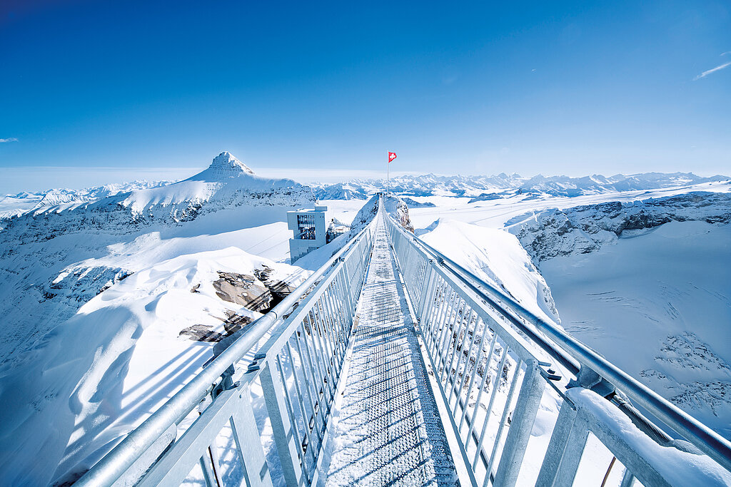 Die Hängebrücke «Peak Walk» auf dem Glacier 3000 vor verschneiter Bergkulisse und Bergrestaurant Botta.